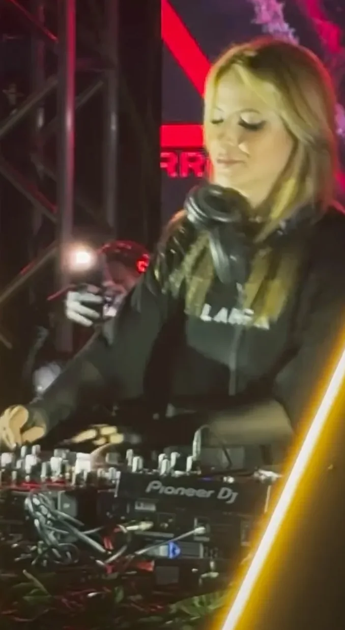 Lahra de moletom preto com a marca LAHRA mixando em um controlador Pioneer sob luz amarela