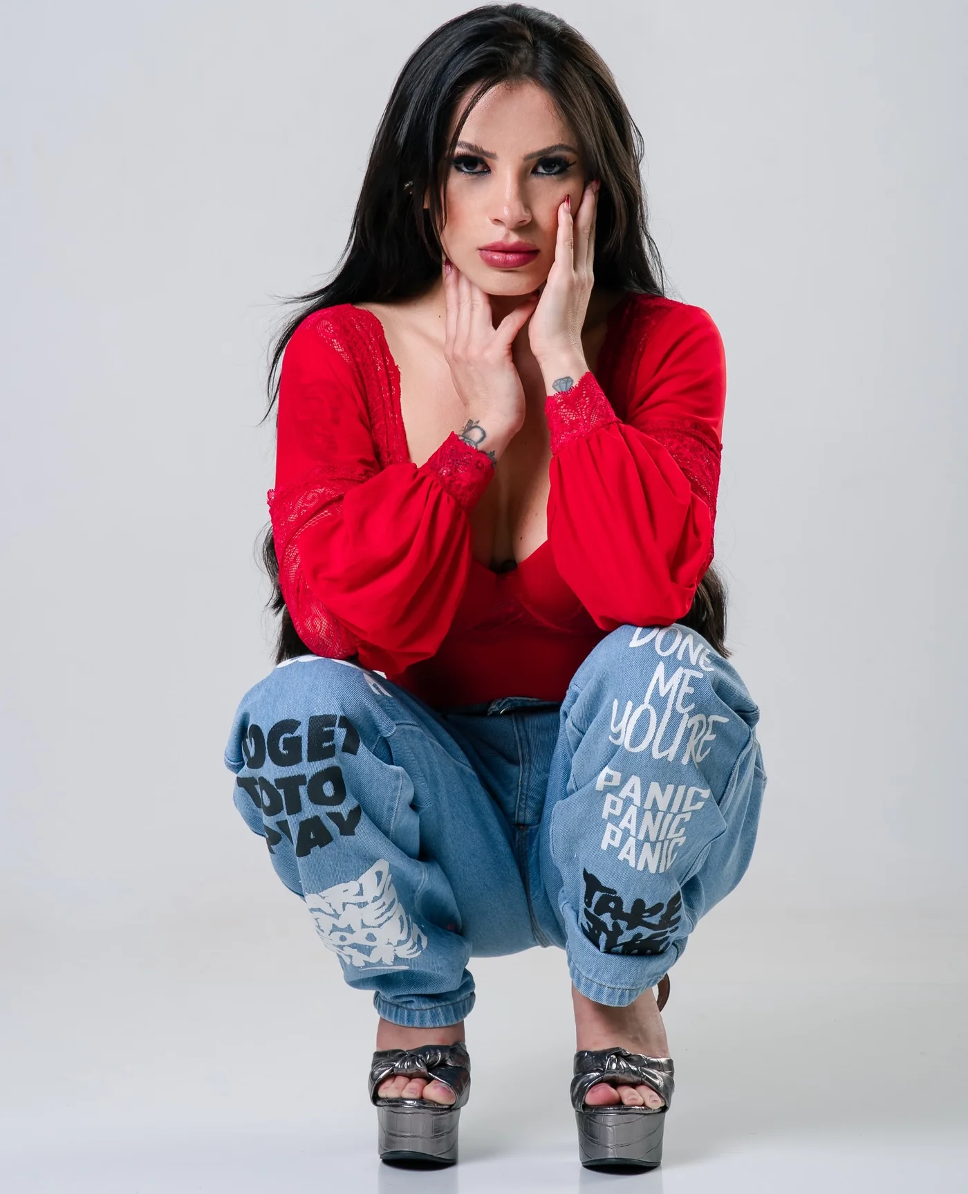 Lahra agachada de body vermelho, calça jeans estampada e plataformas prateadas